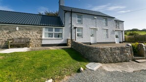 A two-story house with a stone exterior, a metal roof, and a front porch. - Tyn Lon -  a sea view that sleeps 9 guests  in 5 bedrooms (Moelfre)