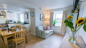 A modern kitchen with white cabinets, a dining table with chairs, a sofa, and a vase with sunflowers. - Tyn Lon -  a sea view that sleeps 9 guests  in 5 bedrooms (Moelfre)