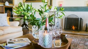 Un salon avec une table basse sur laquelle se trouvent une bouteille, des verres, des magazines et un plateau de noix.