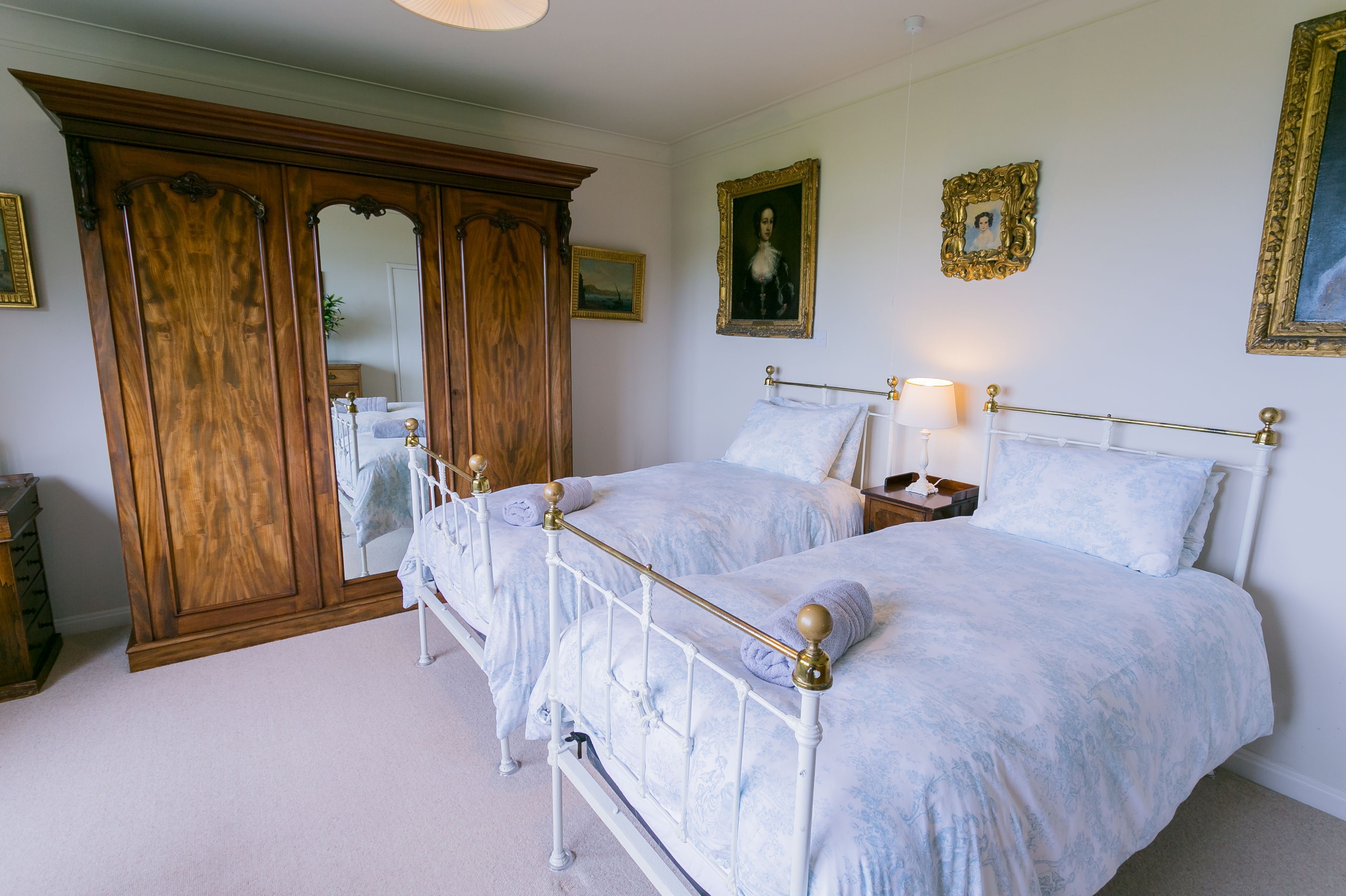 Een slaapkamer met twee bedden, een houten garderobe en een spiegel.