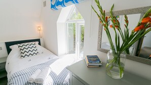 Une chambre à coucher avec un lit, une table de chevet sur laquelle se trouve un livre, un miroir et une fenêtre donnant sur un paysage verdoyant.
