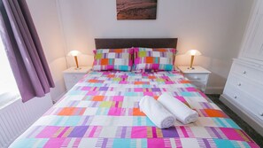 A bed with a colorful quilt, two bedside lamps, and a white towel on the bed.