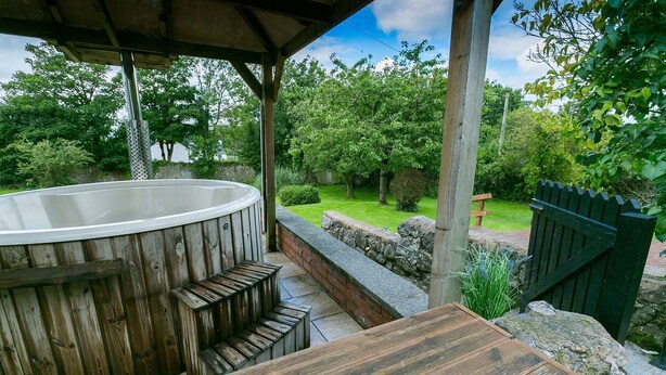 Un bain à remous en bois installé dans un espace abrité, avec un mur en pierre et une terrasse en bois.