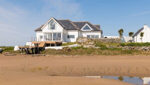 A large white house with a balcony, situated on a sandy beach with a rocky outcrop nearby. - House on the Beach -  an on the beach that sleeps 9 guests  in 4 bedrooms (Holyhead)