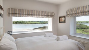 A bedroom with a large bed, two windows with striped valances, a view of a lake, and a framed picture on the wall. - House on the Beach -  an on the beach that sleeps 9 guests  in 4 bedrooms (Holyhead)