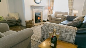 Una sala de estar acogedora con chimenea, dos sofás, una mesa de centro con una botella de champán y una cesta de mimbre.