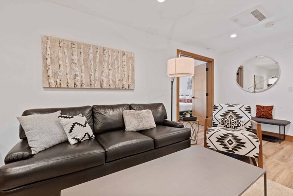 A modern living room with a brown leather sofa, a round mirror, and a large abstract painting on the wall.