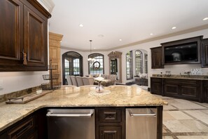 A spacious kitchen with dark wood cabinets, a granite countertop, and a large island with a sink. - Grand Cove - 6 Bdrm Waterfront House with Pool (Sunrise Beach)