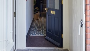 Um corredor estreito com uma porta preta, uma parede branca e um sinal de saída de emergência verde.