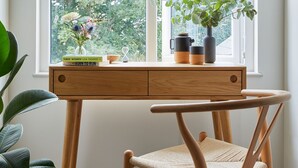 Um quarto com uma janela grande, uma escrivaninha de madeira, uma cadeira e um vaso com planta.