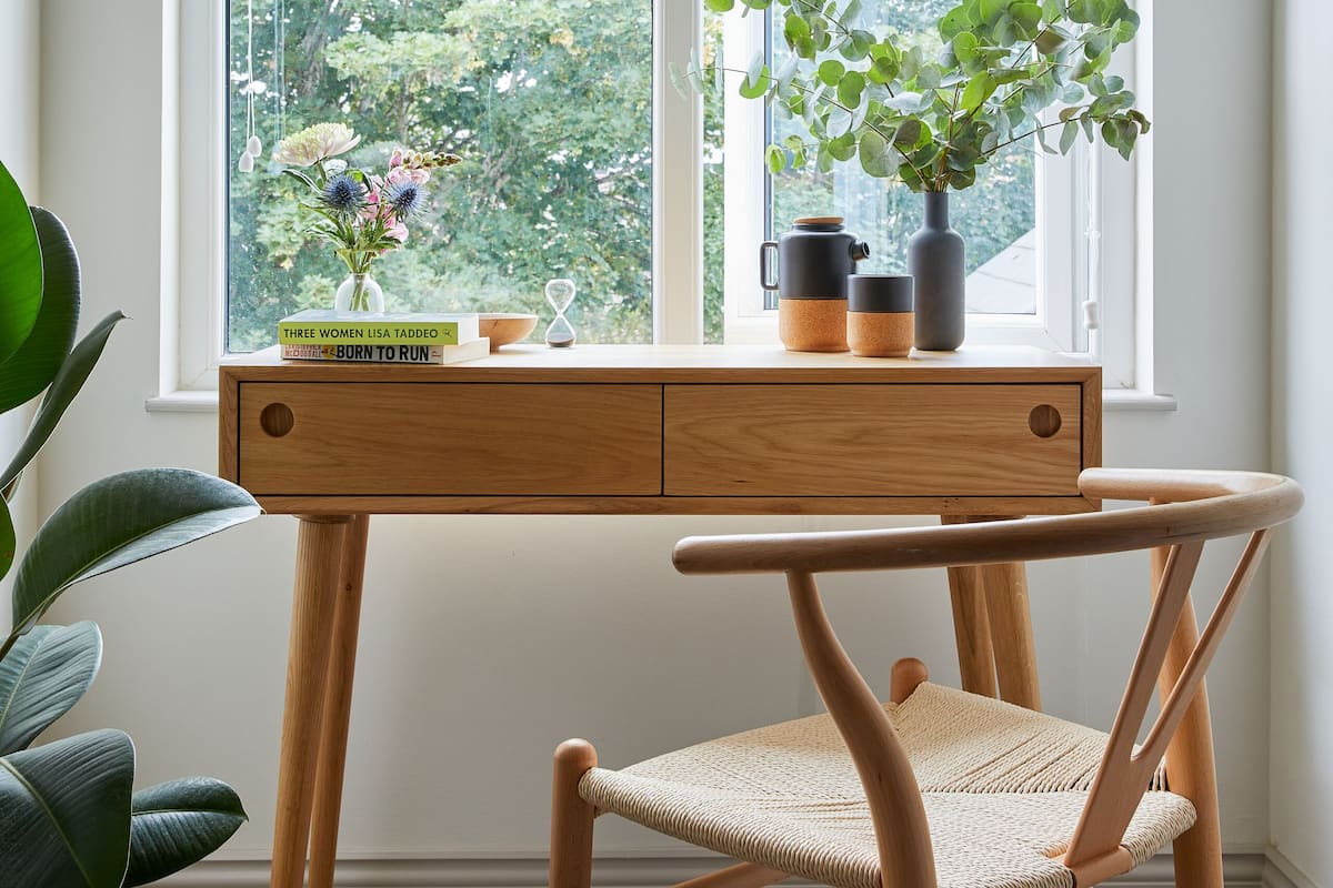 A room with a large window, a wooden desk, a chair, and a potted plant.