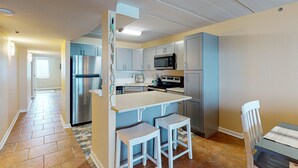 Cocina compacta con refrigerador, microondas, estufa y taburetes de bar.