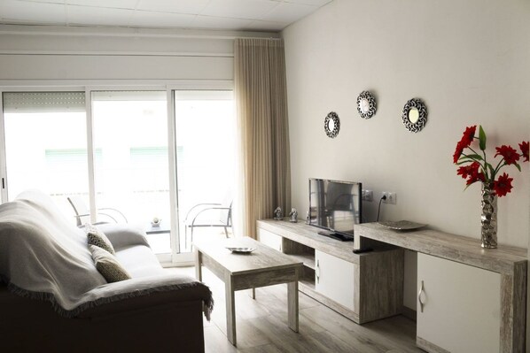 A modern living room with a sofa, a coffee table, a TV, and a dining area.