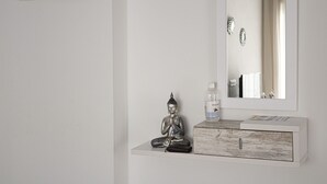 Un baño minimalista con tocador blanco, una estatua de Buda, una botella de jabón para manos y un espejo.