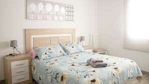 Un dormitorio con cama, mesitas de noche, lámpara y una obra de arte en la pared.