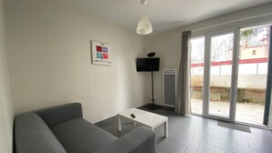 Una sala de estar moderna con un sofá gris, una mesa de centro blanca, un televisor de pantalla plana y una lámpara de pie.