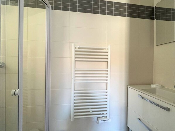 Un baño con un toallero blanco, un box de ducha de vidrio y un lavamanos blanco con un espejo encima.