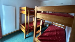 Een slaapkamer met een stapelbed, een radiator, een tafeltje en een groen vloerkleed.