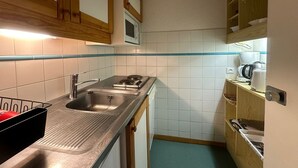 Een kleine keuken met een RVS spoelbak, een magnetron en houten keukenkastjes.
