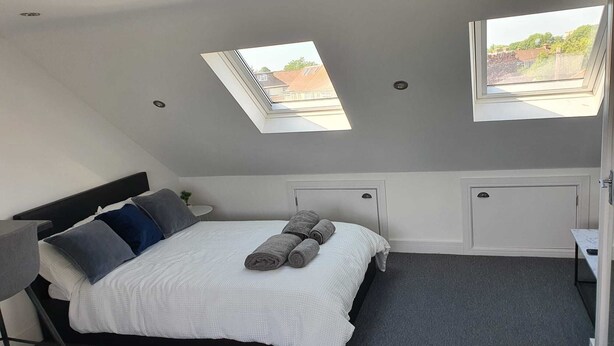 Een moderne slaapkamer met dakraam, een bed met opgerolde handdoeken, een nachtkastje en een klein bureau.