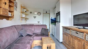 A compact living space with a purple sofa, wooden cabinets, a television, and a kitchen area. - Studio cabin for 4 on slopes with balcony (Belle Plagne)