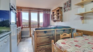 A compact room with a wooden bed, a small table, and a window with curtains. - Studio cabin for 4 on slopes with balcony (Belle Plagne)