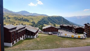 A mountain village with traditional wooden buildings, a clear sky, and a view of distant mountains. - Studio cabin for 4 on slopes with balcony (Belle Plagne)