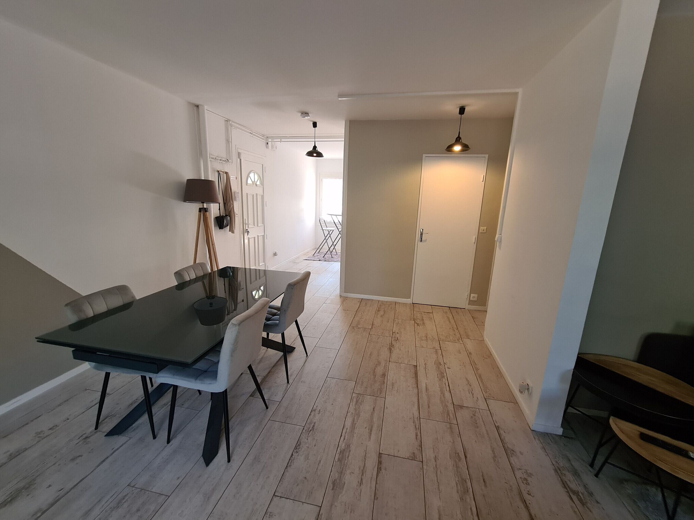 A dining area with a glass table and chairs, a lamp, and a door leading to another room.