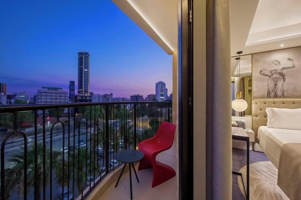 A balcony with a city view, a red chair, a bed, and a lamp.