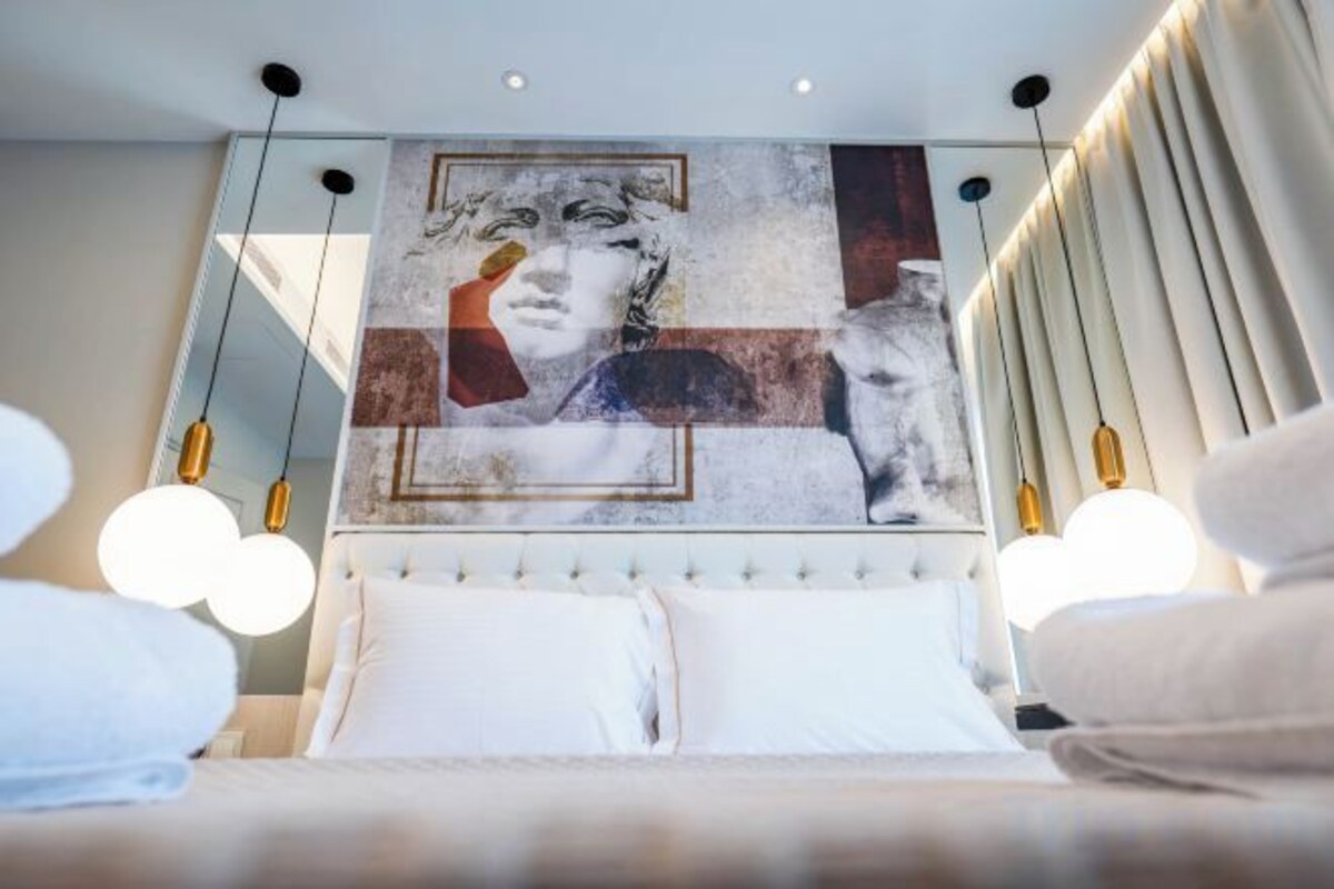 A modern hotel room with a large bed, a headboard with artwork, and two bedside lamps.