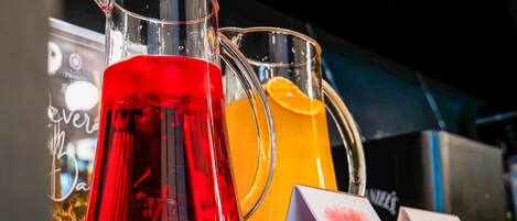 A display of pitchers with red and orange liquids, possibly juices, with labels indicating 'Rose Water' and 'Orange Juice'.