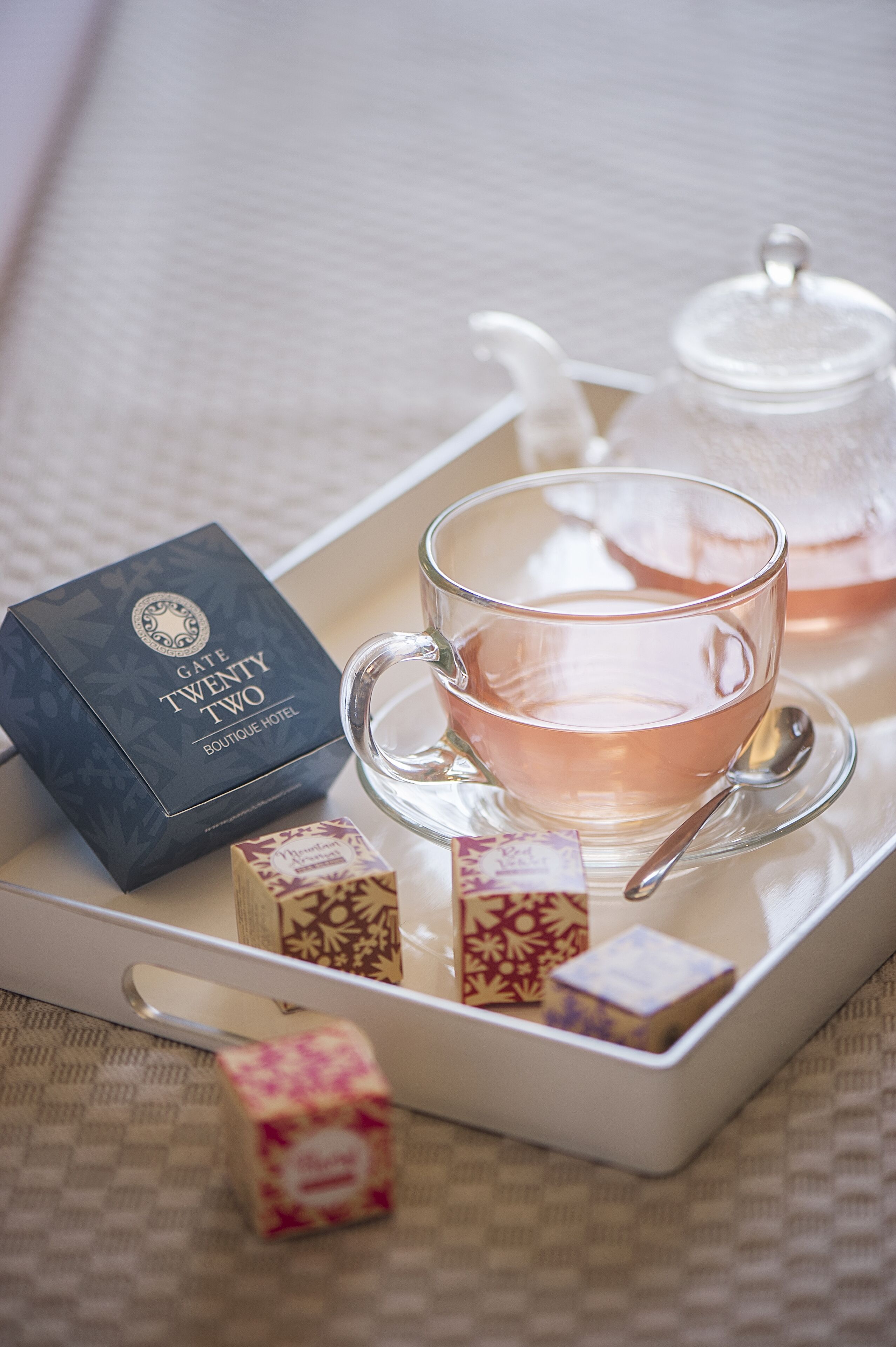 A tray with a glass cup of tea, a teapot, and a box labeled "GATE TWENTY TWO BOUTIQUE HOTEL".