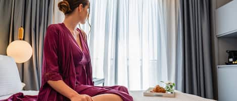 A woman sitting on a bed in a hotel room with a breakfast tray on the side.
