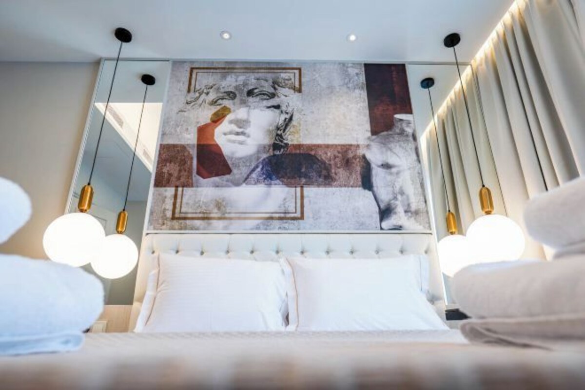 Un dormitorio con una cama grande, cabecera con pintura y lámparas colgantes.