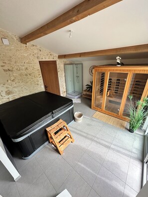 Quarto com sofá preto, um banquinho de madeira, box de vidro para o chuveiro, armário de madeira com portas de vidro e parede de pedra.
