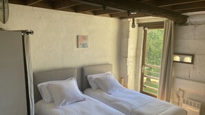 Quarto com duas camas, um ventilador de teto, janela com cortinas e uma pequena imagem na parede.