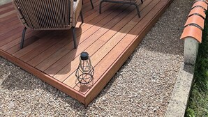 Um pátio externo com móveis de vime, uma mesa e um guarda-sol grande.