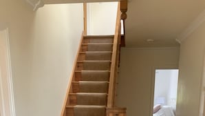 Eine hölzerne Treppe mit Teppichstufen führt zu einem Schlafzimmer mit einem Bett und einem Nachttisch.