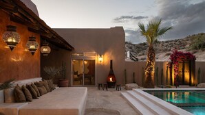 Uma área de estar ao ar livre aconchegante com piscina, lareira e uma palmeira.