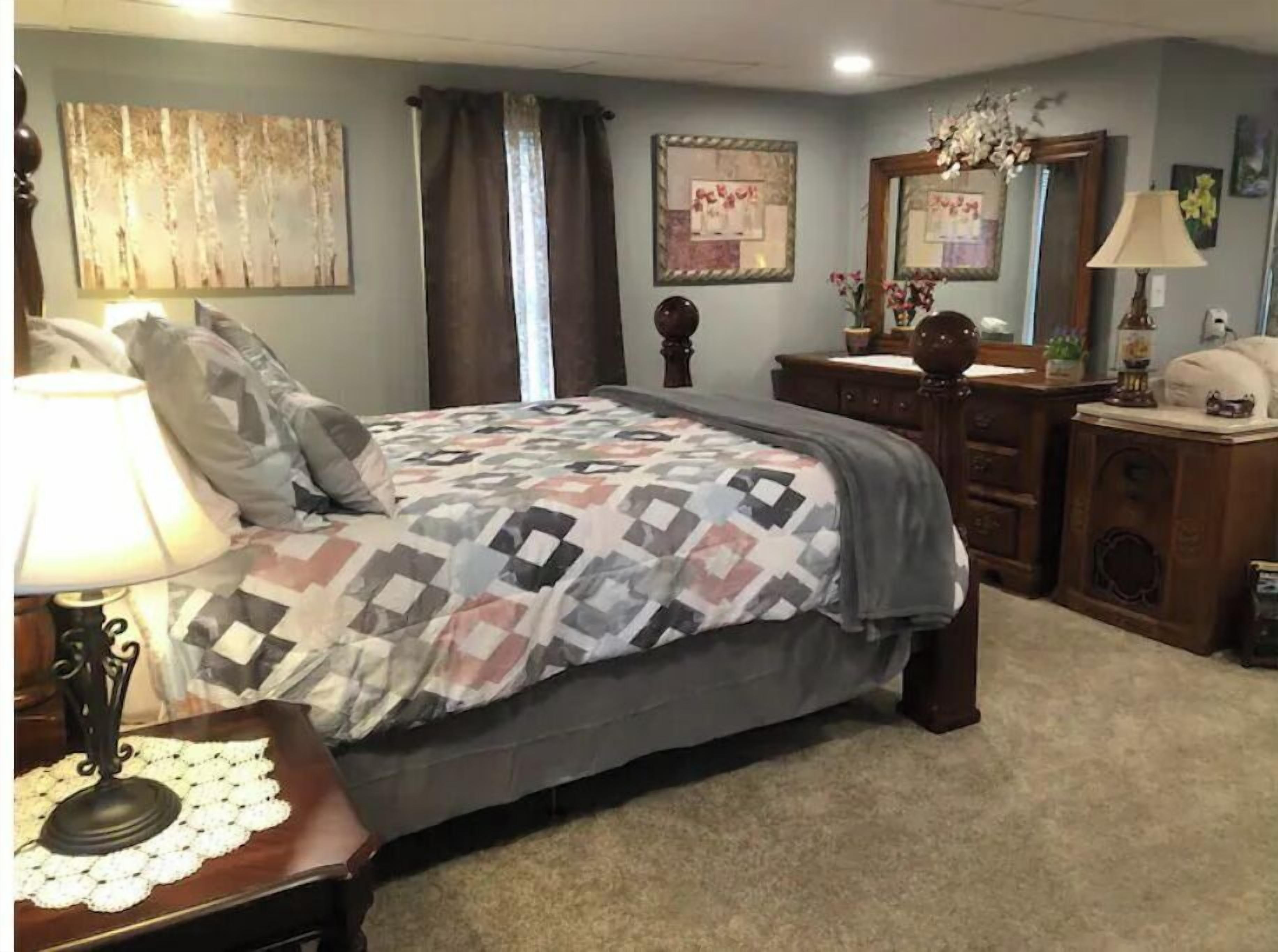 A bedroom with a bed, a dresser, a nightstand, and a lamp.