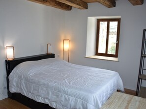 A bedroom with a bed, bedside lamps, a window, and a wooden ceiling.