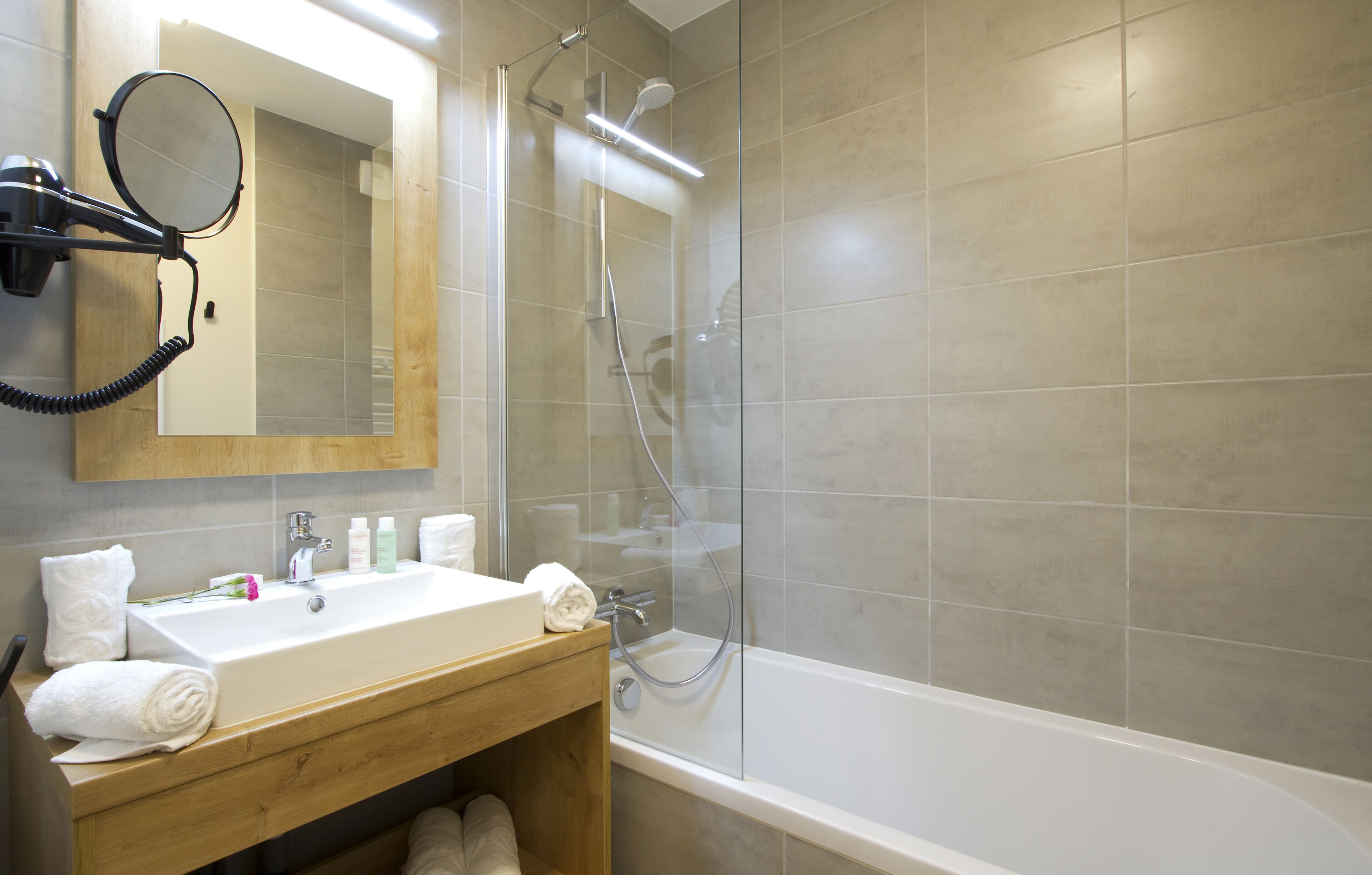 Een moderne badkamer met een grote spiegel, een wastafel, een douche en een haardroger die aan de muur is bevestigd.