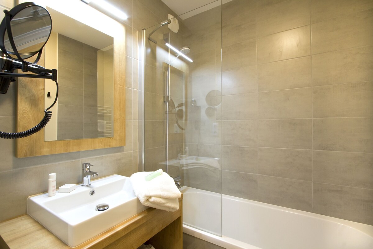 Une salle de bain équipée d’un lavabo, d’un miroir, d’une serviette et d’une douche séparée par des parois en verre.