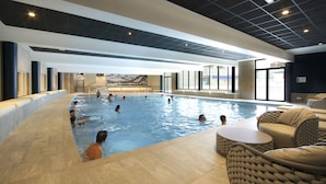 Une piscine intérieure où des personnes nagent et se détendent au bord de l’eau.