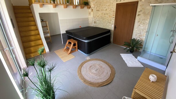A spacious room with a stone wall, a wooden staircase, a black massage table, a glass shower enclosure, and a wooden bench. - Charming gîte "chez Lisa" 91m2 (Saint-Just)