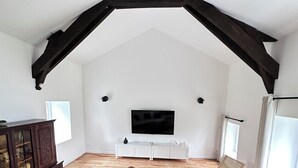 A spacious living room with a high ceiling, wooden beams, a large flat-screen TV, white sofas, a coffee table, and a wooden cabinet. - Charming gîte "chez Lisa" 91m2 (Saint-Just)