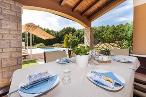 Enjoy a serene dining experience under a shaded pergola with a pool view.