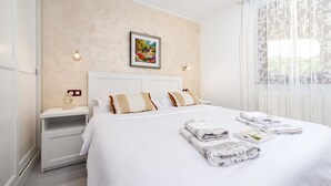 Un lit bien fait, avec du linge de lit blanc et une serviette pliée, une table de chevet avec une lampe et un tableau encadré au mur.