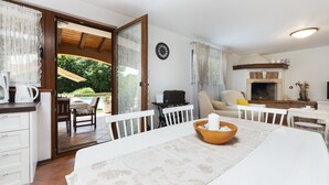 Une pièce comprenant une table à manger, un canapé blanc, une cheminée et donnant sur le jardin.