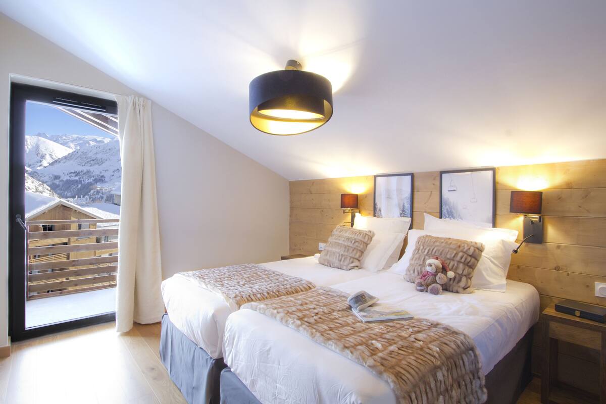Une chambre avec deux lits, une grande fenêtre donnant sur les montagnes, une tête de lit en bois et des lampes fixées au mur.